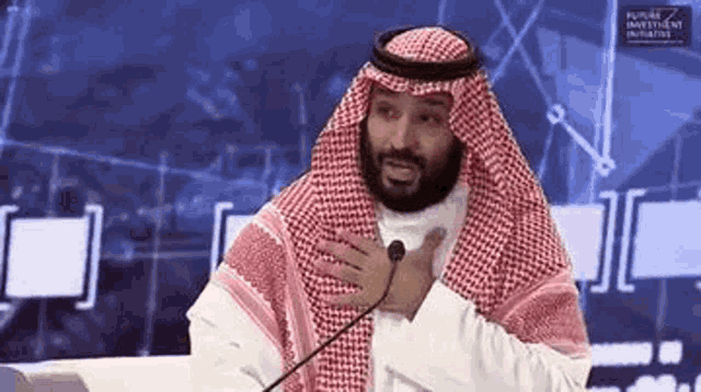 a man in a keffiyeh is talking into a microphone while sitting at a table .
