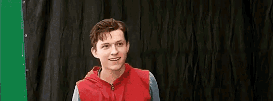 a young man in a red vest is standing in front of a green screen .