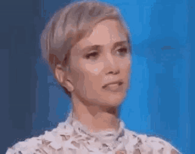 a woman in a white lace dress is making a funny face on a blue background .