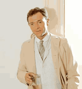 a man in a tan suit and tie is holding a glass of wine