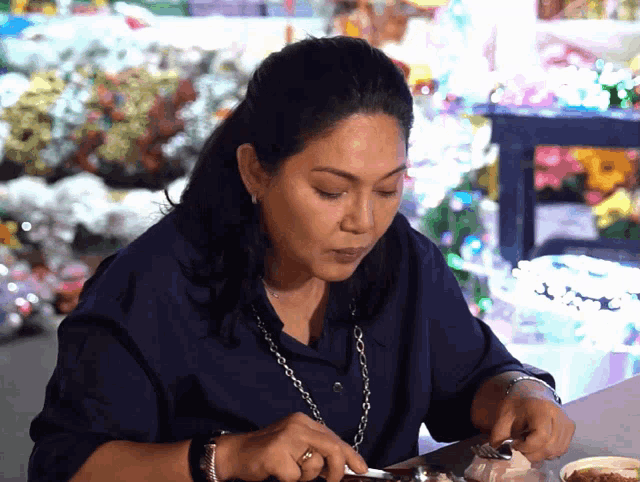 a woman in a blue shirt is cutting a piece of meat