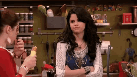 a woman is standing in a kitchen with her arms crossed while another woman is holding a banana .