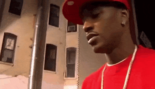 a man wearing a red shirt and a hat is standing in front of a building .