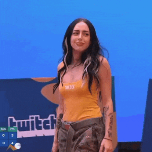 a woman in a yellow diesel tank top is standing in front of a twitch screen .