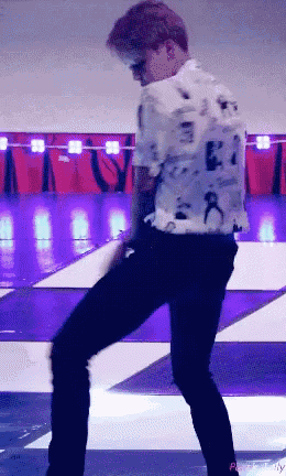 a man in a white shirt is dancing on a stage with purple lights behind him
