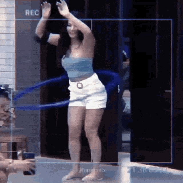 a woman in a blue top and white shorts is dancing with a blue hula hoop ..