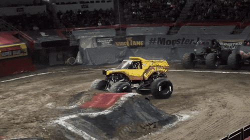 a yellow monster truck is driving on a dirt track in front of a monster jam sign