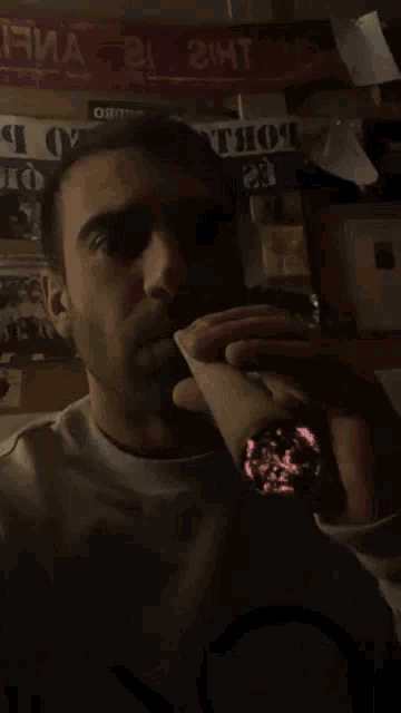 a man is drinking from a cup in front of a sign that says ' the 24t '