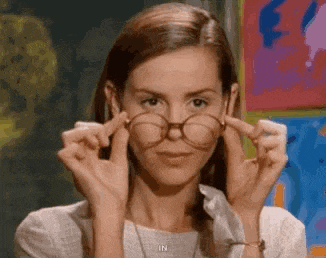 a woman is adjusting her glasses in front of a painting in a classroom .