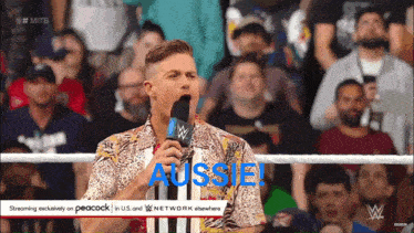 a man in a hawaiian shirt is speaking into a microphone with the word aussie on the screen