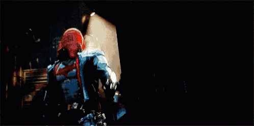 a person in a red hooded jacket is holding a gun that is shooting a lot of light rays .