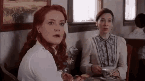 two women are sitting at a table with a cup of tea and a plate of food .