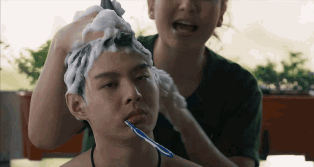 a woman is washing a boy 's head with soap and a toothbrush