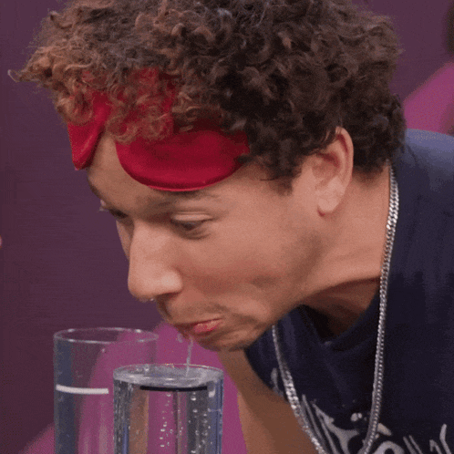 a man with curly hair wearing a red headband looks down at a glass of water
