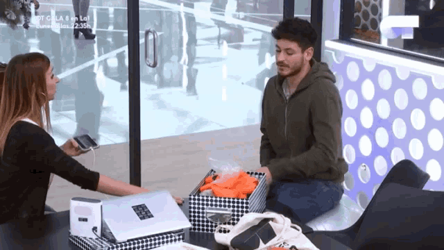 a man and a woman are sitting at a table in front of a window with a sign that says cola