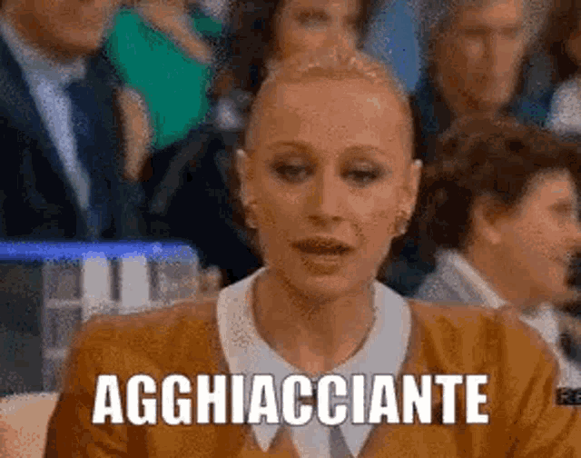a woman in a brown sweater is sitting in front of a crowd of people and says agghiacciante .