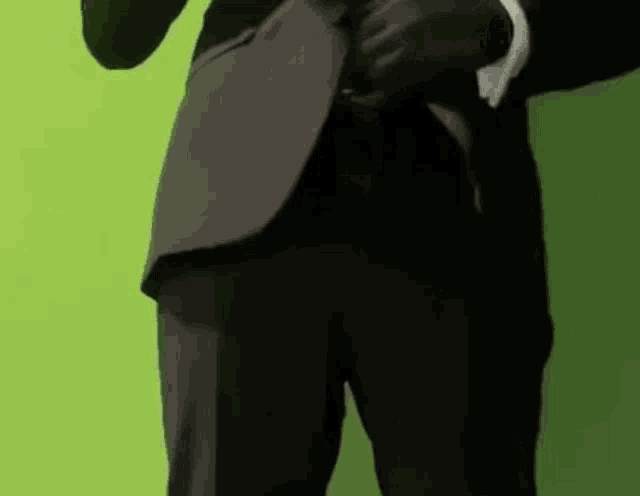 a man in a suit is standing in front of a green background and adjusting his jacket .
