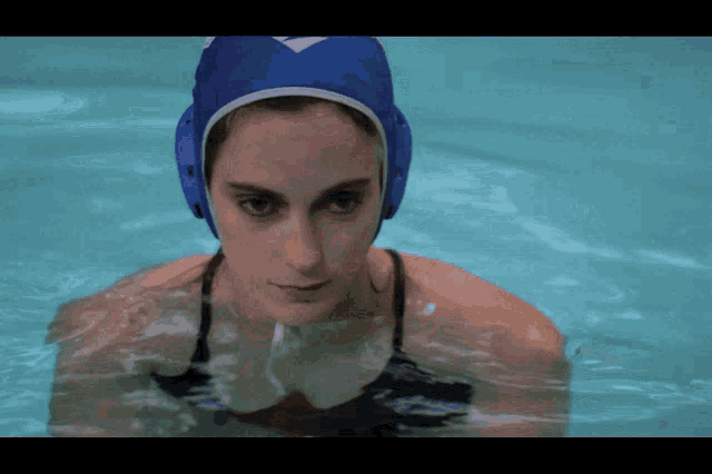 a woman wearing a blue water polo helmet is swimming