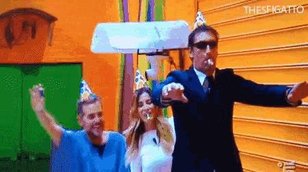 a man in a suit is blowing a party horn while a woman in a party hat watches .