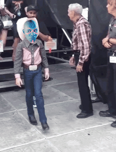a little boy in a cowboy outfit has a blue face painted on his head