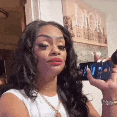 a woman is holding a phone in front of a dior poster