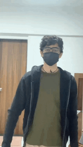 a man wearing a black mask and glasses is standing in a room .