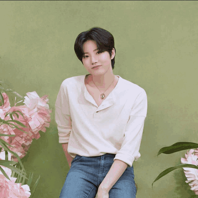 a man wearing a white shirt and blue jeans is sitting in front of flowers