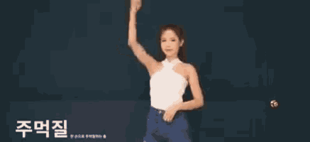 a woman in a white tank top and blue shorts is dancing in front of a black wall .