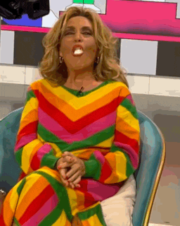 a woman in a colorful sweater is sitting in a chair with her mouth open and a candy in her mouth .