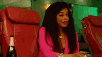 a woman in a pink jacket is sitting in a red chair with a bottle of champagne in front of her .