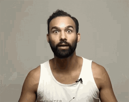 a man with a beard wears a white tank top that says unlimited