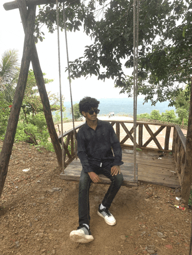 a young man sits on a wooden swing with a view of the ocean