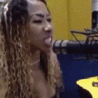 a woman with long curly hair is sticking her tongue out while sitting in front of a yellow wall .