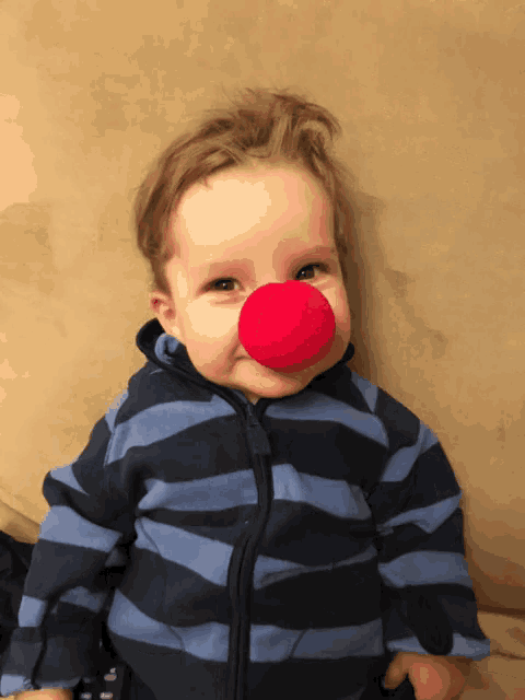 a baby wearing a blue and black striped jacket has a red nose