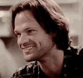 a man with long hair and a beard is smiling and looking at the camera .