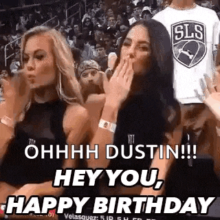 two women are sitting in the stands at a basketball game and one is blowing a kiss .