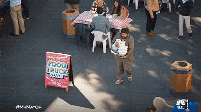 a man carrying a tray of food stands in front of a sign that says food truck day