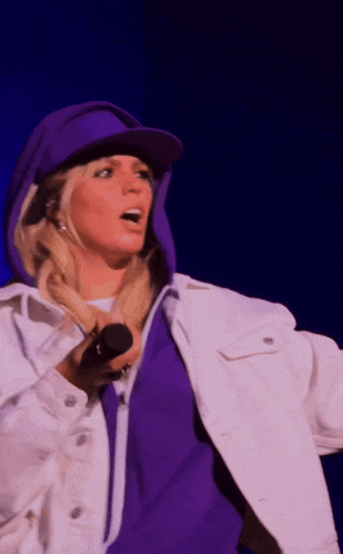 a woman singing into a microphone wearing a purple hat and a white jacket