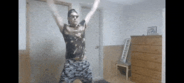 a man wearing sunglasses and a hat is dancing in a room .