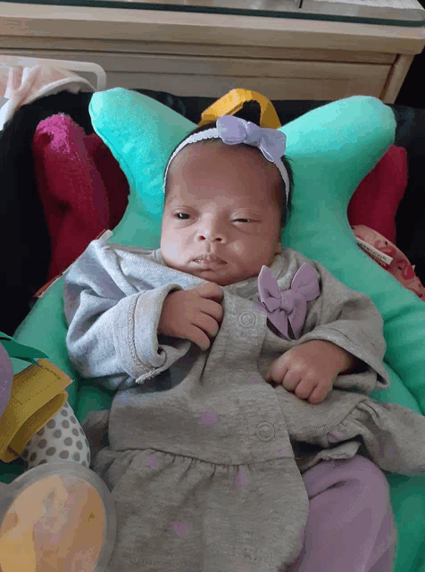 a baby wearing a gray and purple outfit with a bow