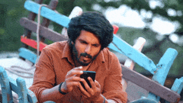 a man in a brown shirt is looking at his phone