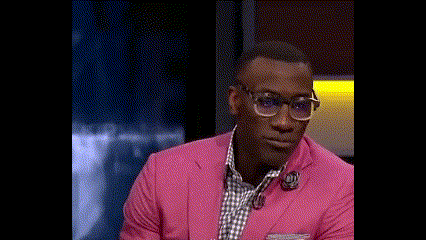 a man wearing a pink suit and glasses is smiling while sitting on a stage .