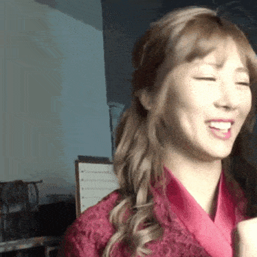 a woman in a pink robe is smiling with her eyes closed and wearing a pink robe .