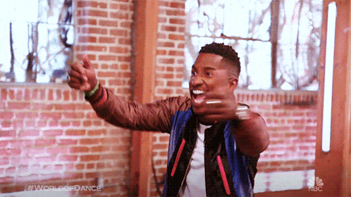 a man is giving a thumbs up in front of a brick wall and the word world of dance is on the bottom