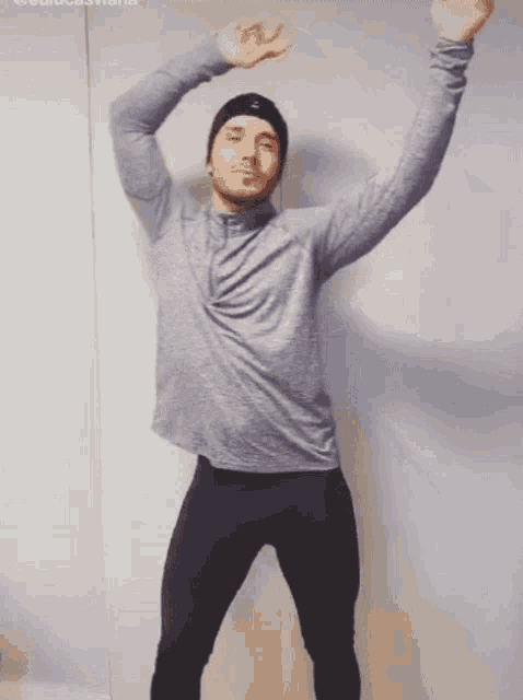 a man in a gray shirt and black pants is dancing with his hands in the air .