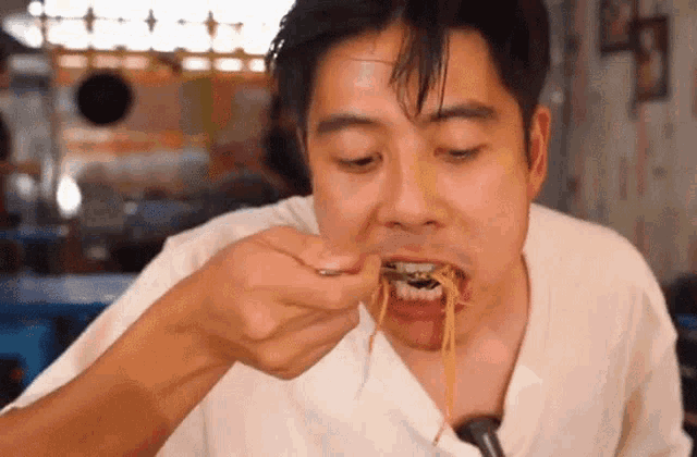 a man is eating noodles with a spoon and fork
