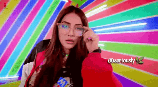 a woman wearing glasses and a red jacket is standing in front of a colorful background that says @seriously