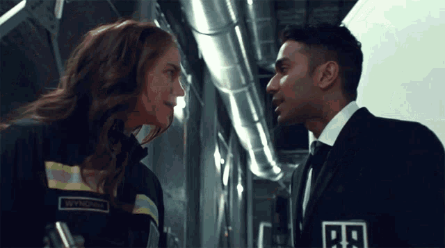a man and a woman are facing each other and the man has a badge that says b9