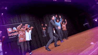 a group of men are dancing on a stage in front of a dance comp sign