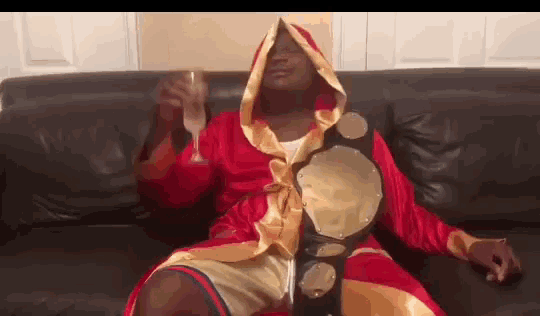 a man in a boxing robe is sitting on a couch drinking a glass of champagne